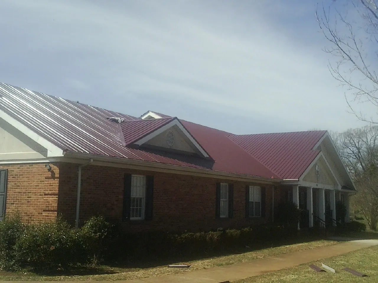 Red metal roof with gabled entries on a long brick building, from a Hail Damage Roof Repair job in Fredericktown