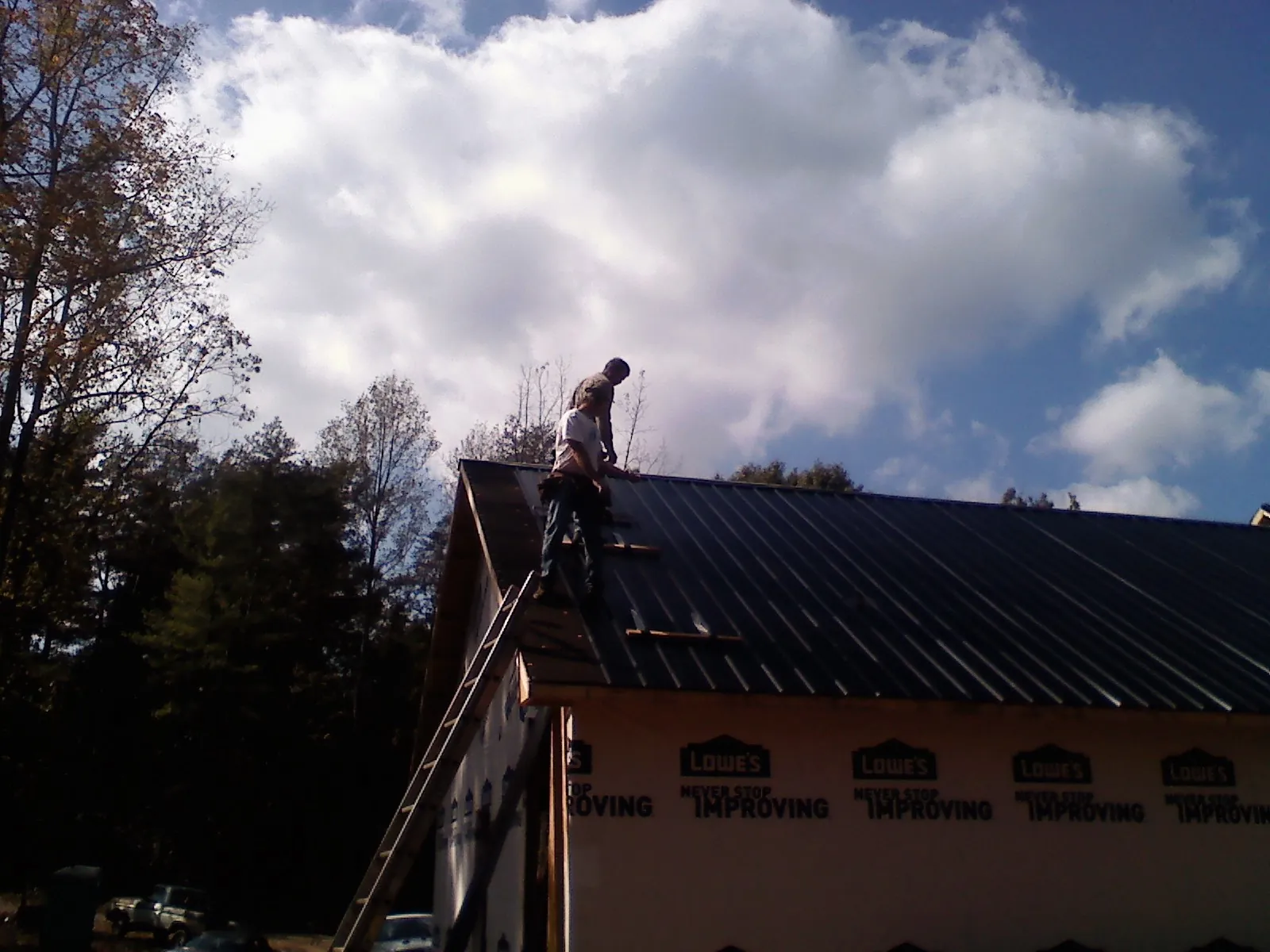 Roofer fastening dark metal panels high against a cloudy sky, from a Roof Inspection job in Fredericktown