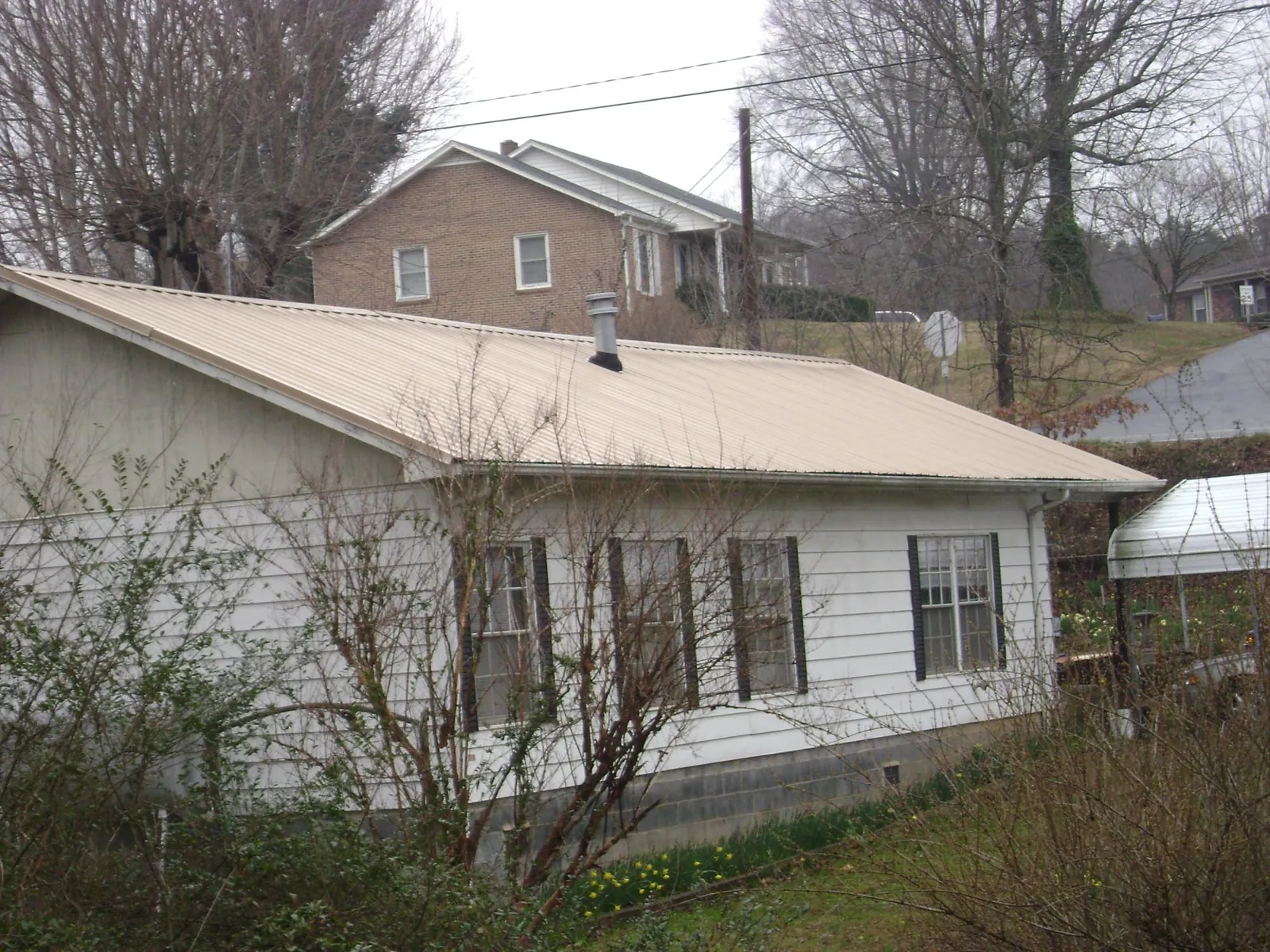 Tan metal roof on a white sided house set into a hillside — Commercial Roofing by Roofing Brothers in Fredericktown